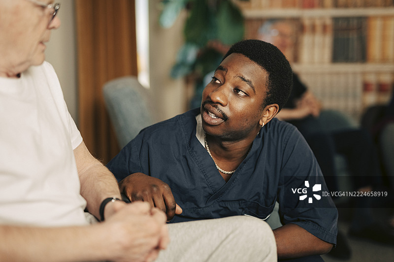 年轻男性护理助理在养老院安慰坐在轮椅上的老人图片素材