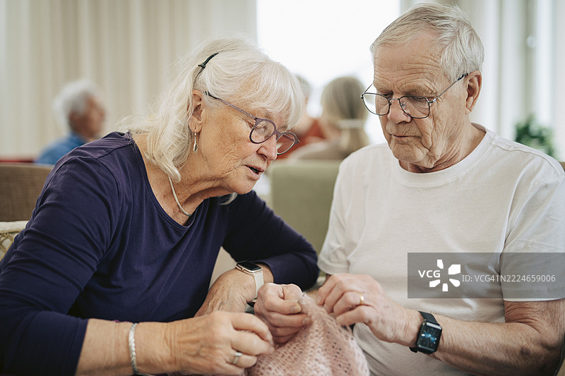退休之家里，年长女性在帮助男性朋友编织。图片素材