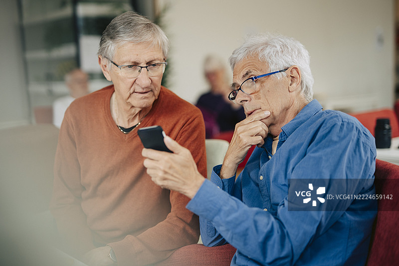 退休的老年男性在养老院里与朋友分享智能手机。图片素材