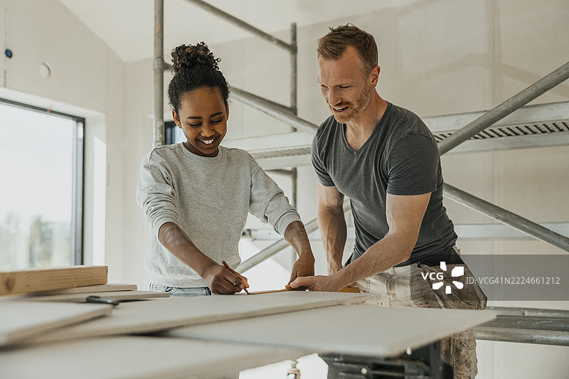 微笑的女孩在父亲的帮助下测量木板的尺寸，进行房屋装修。图片素材