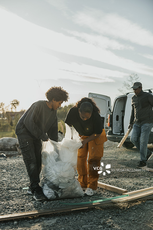 母亲和儿子在阳光明媚的日子里在房子外收集建筑垃圾，装进垃圾袋里图片素材