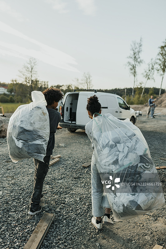 背影中的兄弟姐妹走着，手里提着装有建筑垃圾的垃圾袋图片素材