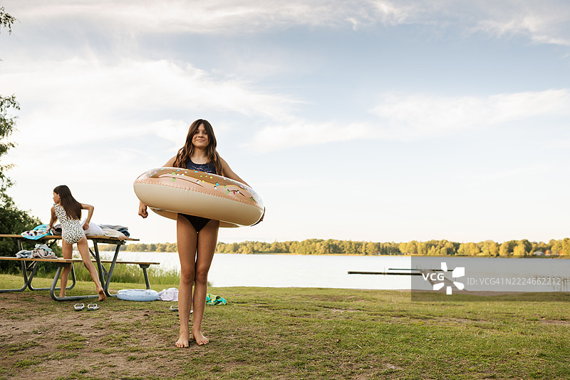 一个女孩拿着游泳圈，另一个女孩在夏天的傍晚海滩上换泳衣。图片素材