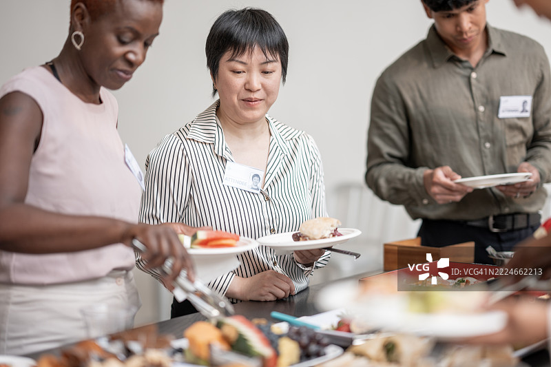 同事们在自助餐桌前聚集，参加会议餐饮活动图片素材