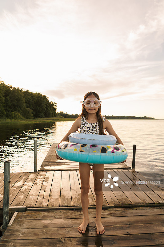 夏天傍晚，湖边一个女孩穿着两个游泳圈的肖像。图片素材