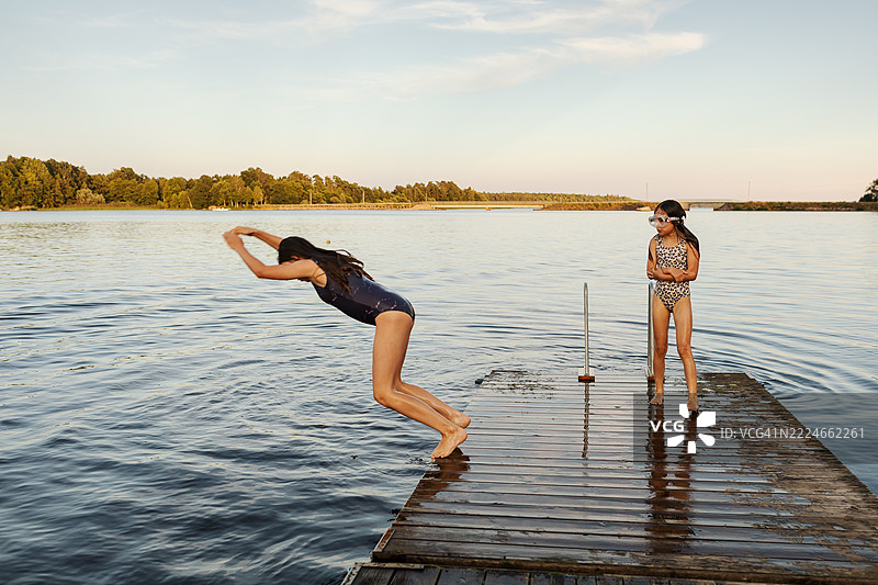 两个女孩在夏天的傍晚从湖边的浴场跳入水中。图片素材