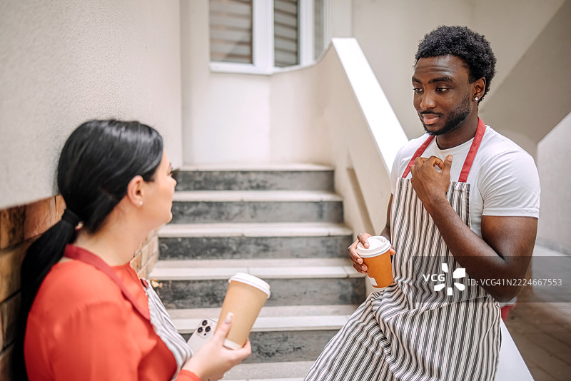 同事们在咖啡馆的楼梯上一起站着休息，享受咖啡时间。图片素材