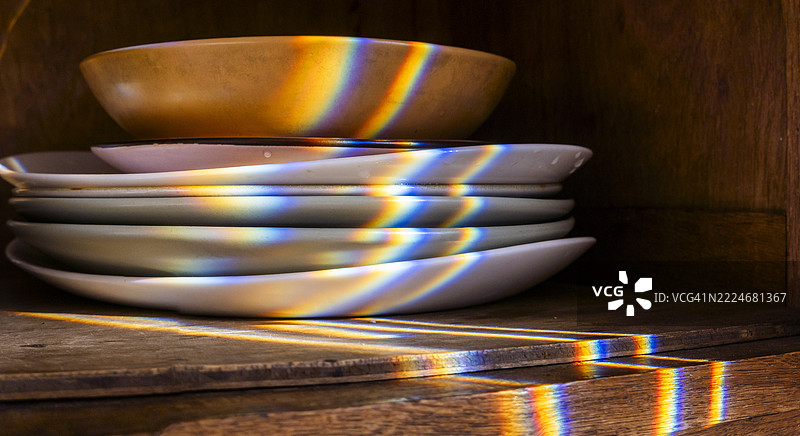 彩虹光线照射在木橱柜中的叠放盘子上图片素材