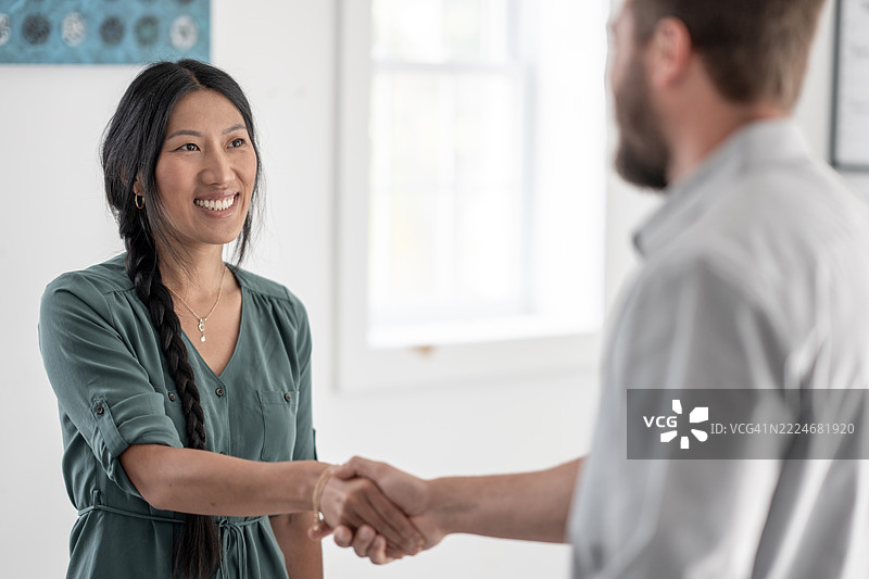 微笑的女商人与一位专业人士在明亮的办公室空间握手图片素材