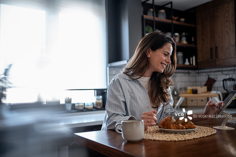年轻女性在现代厨房享用早餐并在平板电脑上浏览互联网图片素材