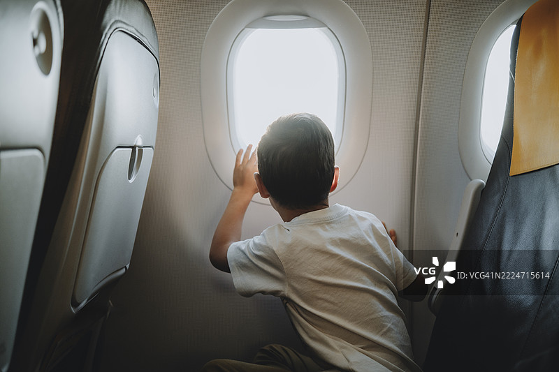 孩子在飞机窗外望着广阔的天空和蓬松的云朵，进行着长途旅行。图片素材