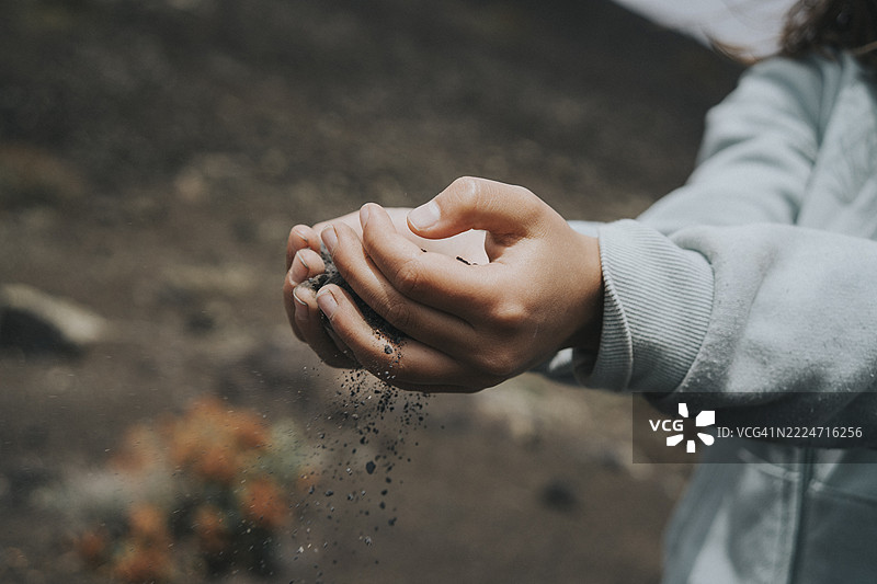 手在筛选火山黑沙，揭示兰萨罗特加那利群岛蒂曼法亚国家公园月球般地形的地质纹理图片素材