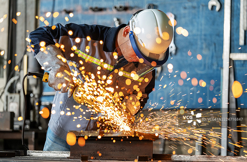 经验丰富的工程师穿着防护工作服、护目镜和面罩，正在使用工业设备对钢制工件进行磨削。火花四溅，突显了重工业和金属加工中的技能、精确度和工作场所安全。图片素材
