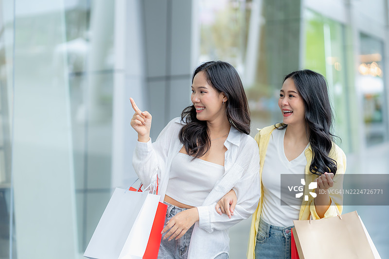 两个快乐的亚洲女性手提购物袋在户外散步图片素材