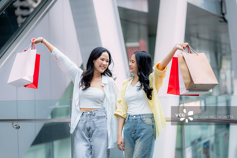 两位亚洲女性微笑着在现代购物中心提着购物袋图片素材