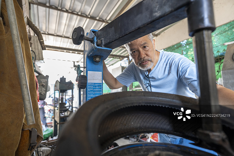老年男性机械师在车间使用轮胎机工作图片素材