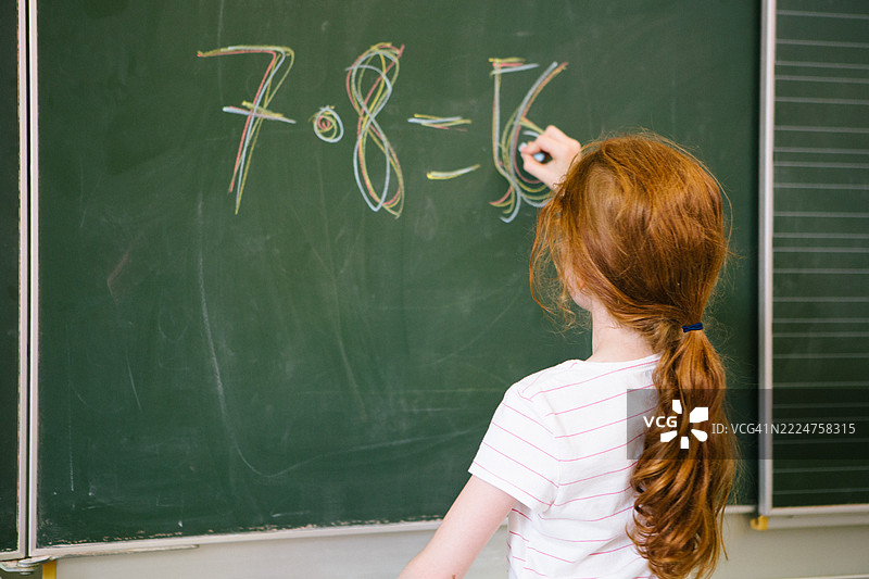 可爱的红发女学生在教室黑板上解数学题图片素材