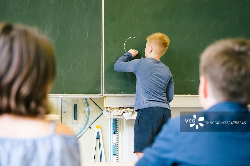 可爱的男学生在教室黑板上解数学题图片素材