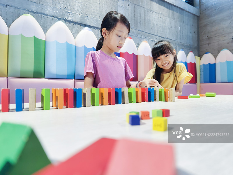 两个亚洲女孩正在玩多米诺骨牌。排列多米诺骨牌需要耐心，并能训练孩子们的专注力。图片素材