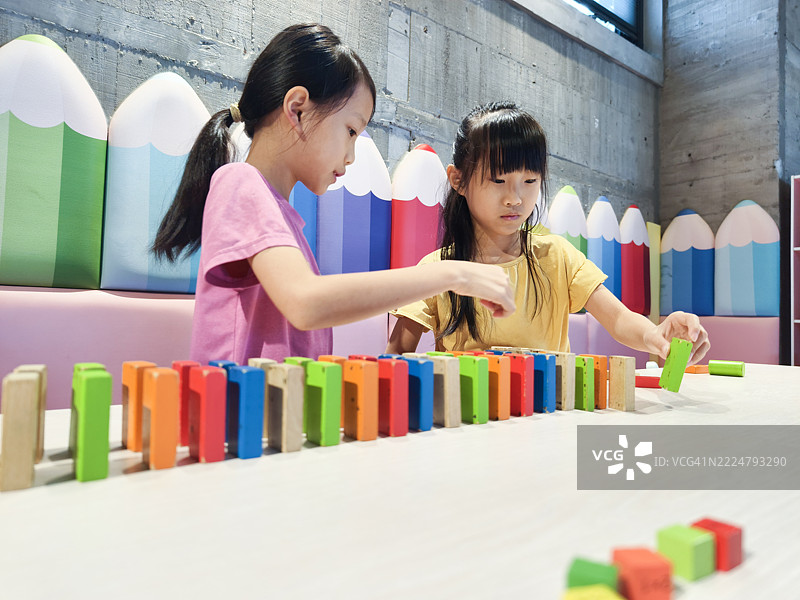 两个亚洲女孩正在玩多米诺骨牌。排列多米诺骨牌需要耐心，并能训练孩子们的专注力。图片素材