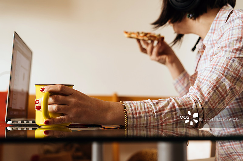 女性在桌子上远程工作，手里拿着茶杯和快速小吃图片素材