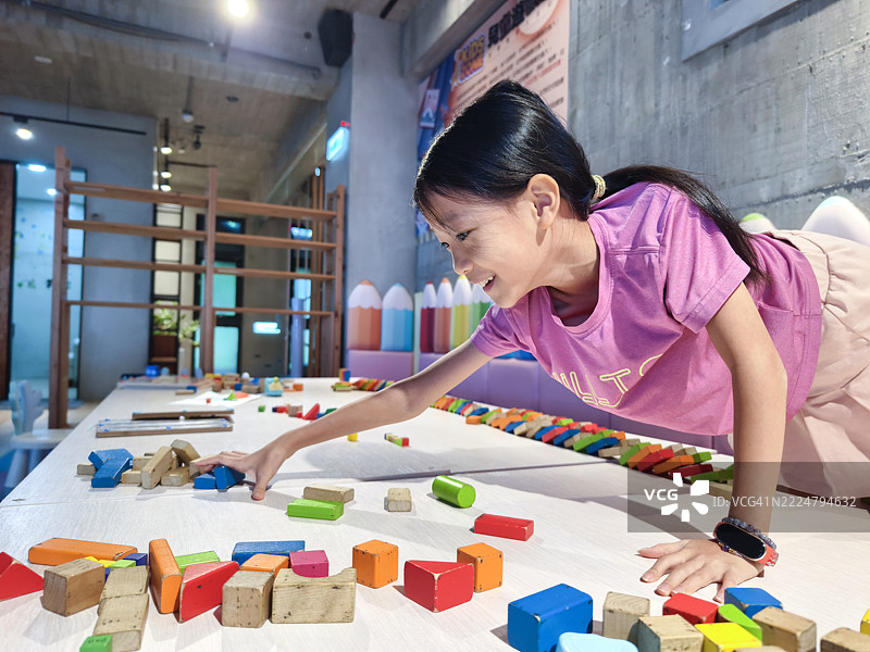 一个亚洲女孩正在玩多米诺骨牌。排列多米诺骨牌需要耐心，并能训练孩子们的专注力。图片素材