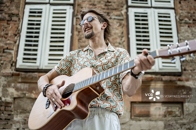 在旧砖建筑附近的户外弹奏原声吉他的男人图片素材