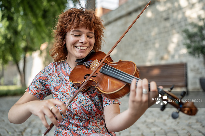 阳光明媚的户外，微笑的女性在快乐地拉小提琴图片素材