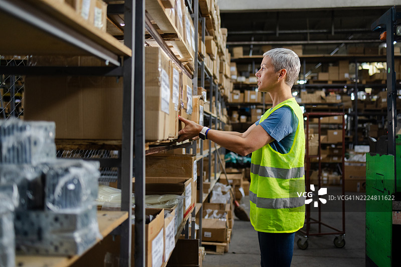 女性仓库工人在检查货架上的纸箱图片素材