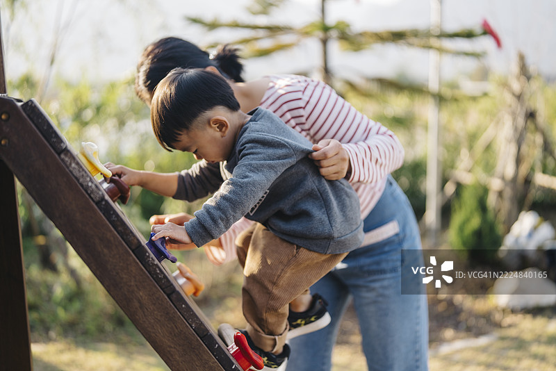 一位亚洲母亲和她的小男孩在户外游乐场攀爬木梯，享受着阳光明媚的活跃一天。图片素材