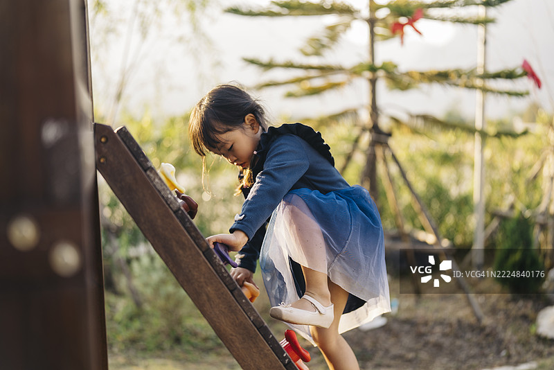 一个小女孩在户外游乐场小心翼翼地走过绳索桥，享受着阳光下有趣而冒险的一天。图片素材