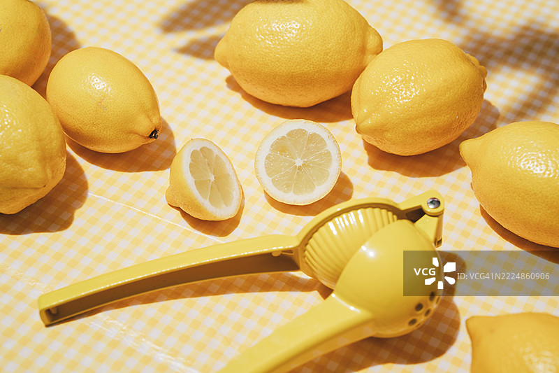 花园桌上放着几颗新鲜的柠檬，铺着黄色桌布。夏季花园。柠檬压榨器和削皮器。柠檬水。图片素材