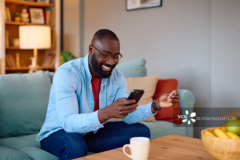 微笑的男人在家中使用智能手机和信用卡进行在线购物图片素材