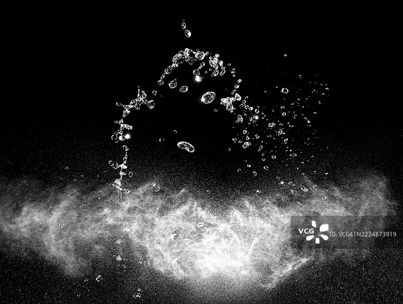 黑色背景上喷洒的水滴和水花的云朵，伴随着移动的水滴。图片素材
