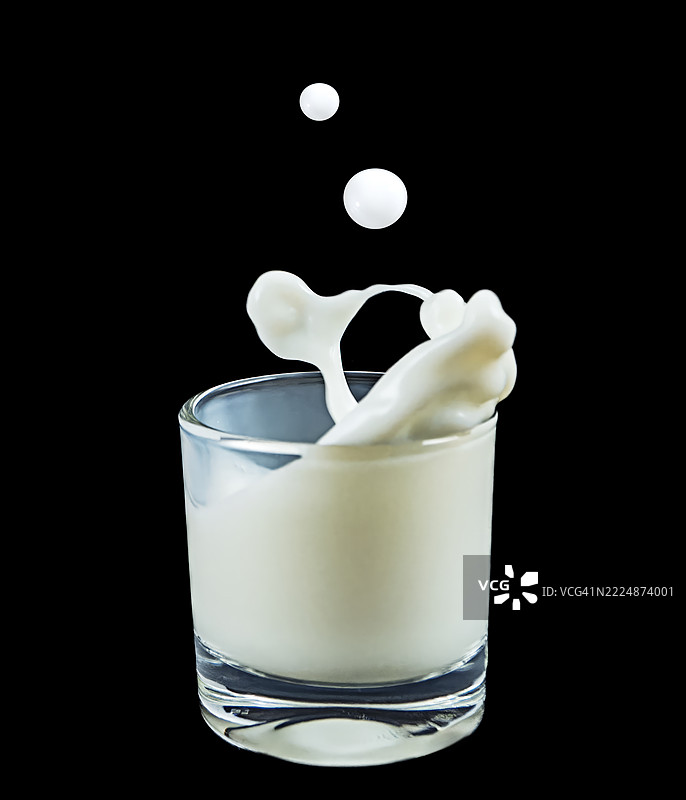 黑色背景上溅出的牛奶杯。图片素材
