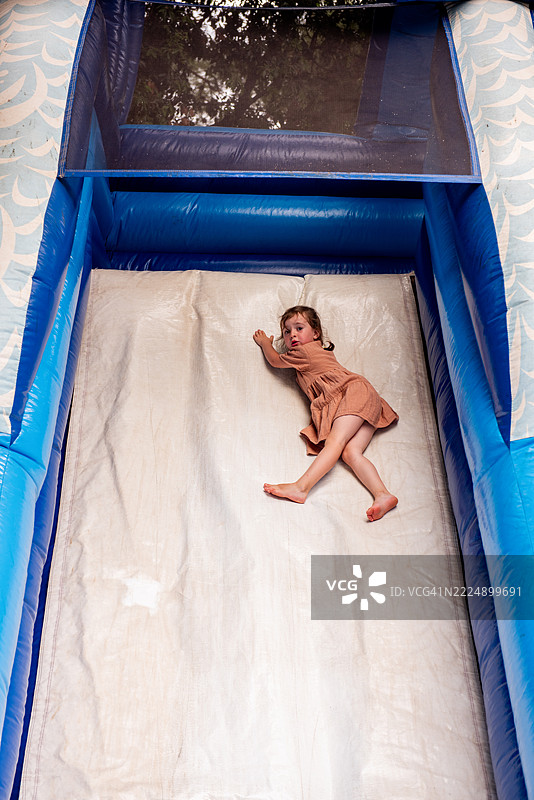 小女孩在游乐场的充气滑梯上滑下去图片素材