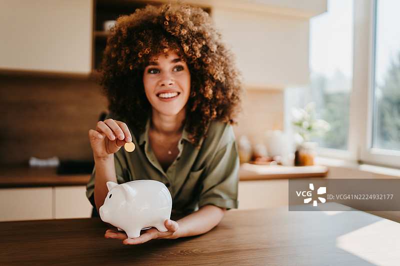 年轻女性在家中把钱存进储蓄罐图片素材