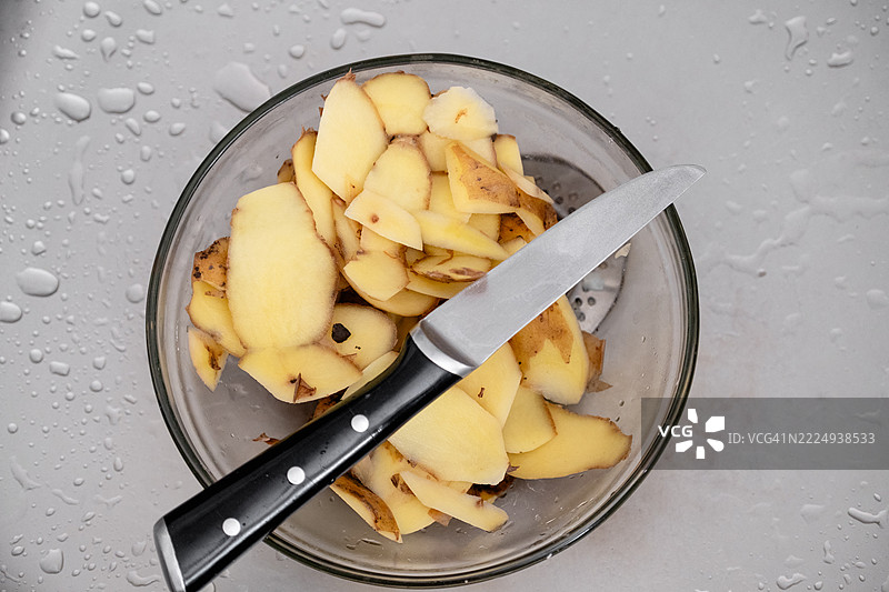 剥皮后的土豆皮放在水槽中的碗里。图片素材