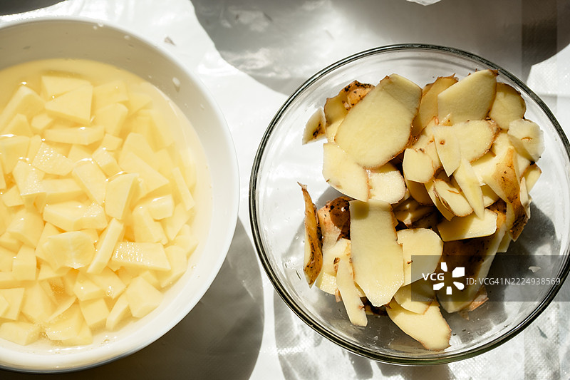 剥皮并切成块的土豆和皮在水中的碗，俯视图图片素材