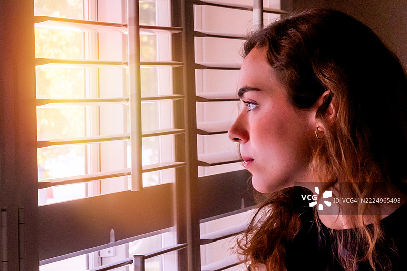 严肃的年轻女性透过家里的窗户向外看图片素材