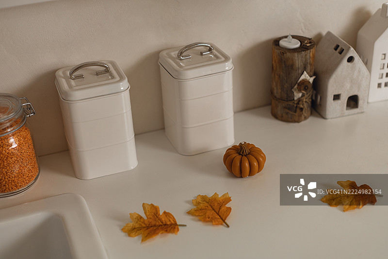 秋季厨房装饰着秋叶、小南瓜、白色罐子、迷你房屋和装在玻璃罐中的扁豆。图片素材