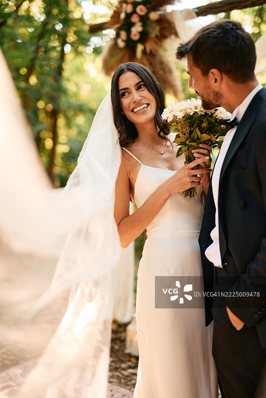 幸福的新娘在婚礼仪式上手捧花束，注视着新郎。图片素材