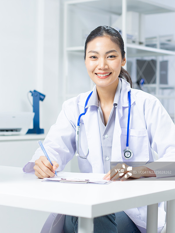 微笑着看向镜头的亚洲女性医生，佩戴听诊器，站在医院的医生办公室里。图片素材
