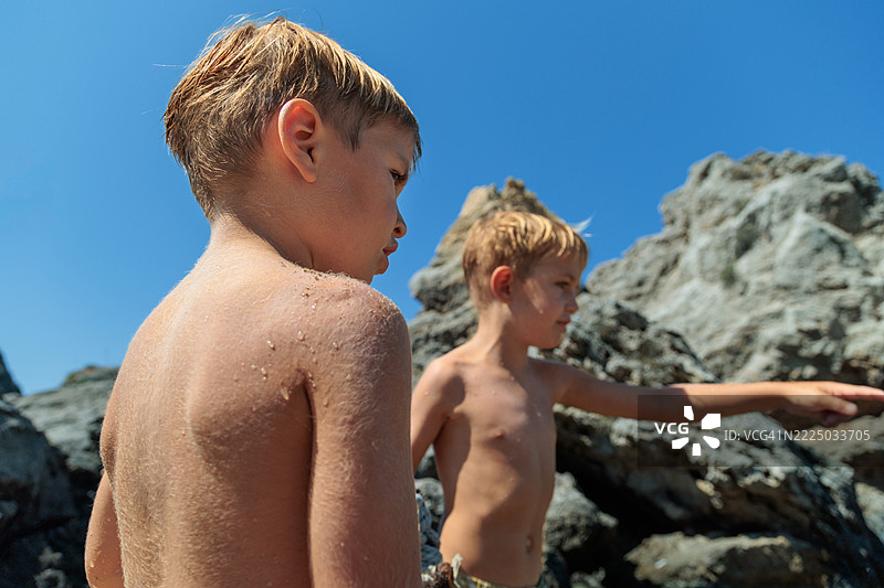 两个年轻的兄弟在岩石海滩上。阳光明媚的夏日海滩假期冒险。图片素材