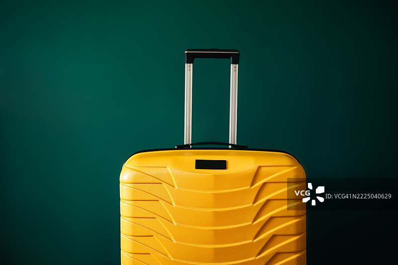明亮的黄色硬壳行李箱，配有伸缩手柄，背景为深绿色，象征着旅行或出发。图片素材