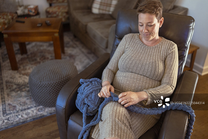 无忧无虑的孕妇坐在扶手椅上织毛线，想为即将到来的宝宝制作一条厚实柔软的毯子图片素材