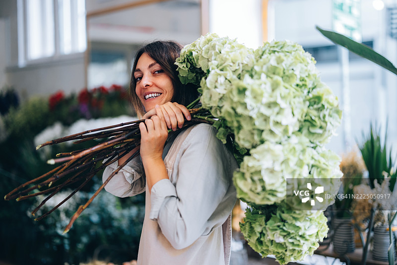 微笑的女性在花店里手捧一大束绿色花卉图片素材