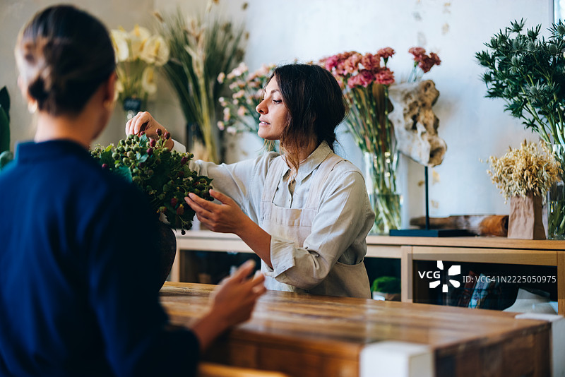 花店柜台上，花店老板一边为顾客服务，一边整理花卉。图片素材