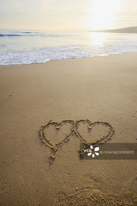 在理想的日落时分，沙滩上画着两个心形图案图片素材