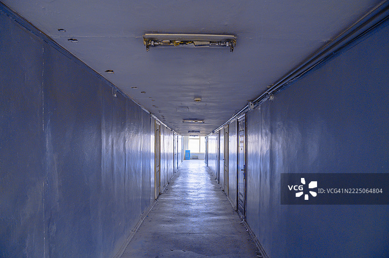 长长的深蓝色走廊，门和荧光灯照亮了整个场景图片素材
